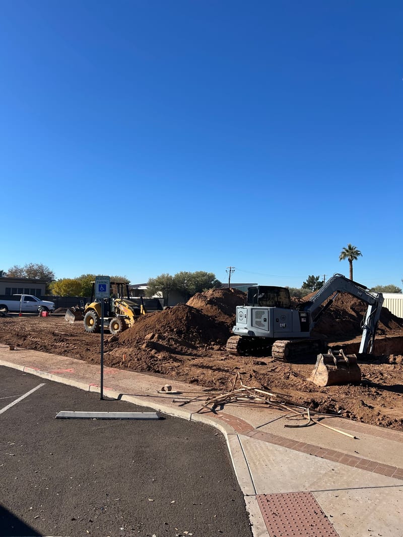 An excavator and loader moving dirt on the cleared Jefferson House lot, December 2025