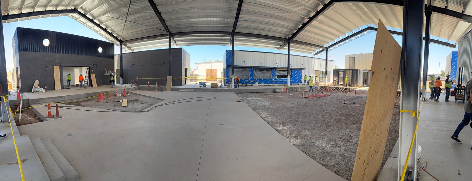 The covered Jefferson House courtyard under its black-steel canopy with the slab poured and shops around it, June 2026